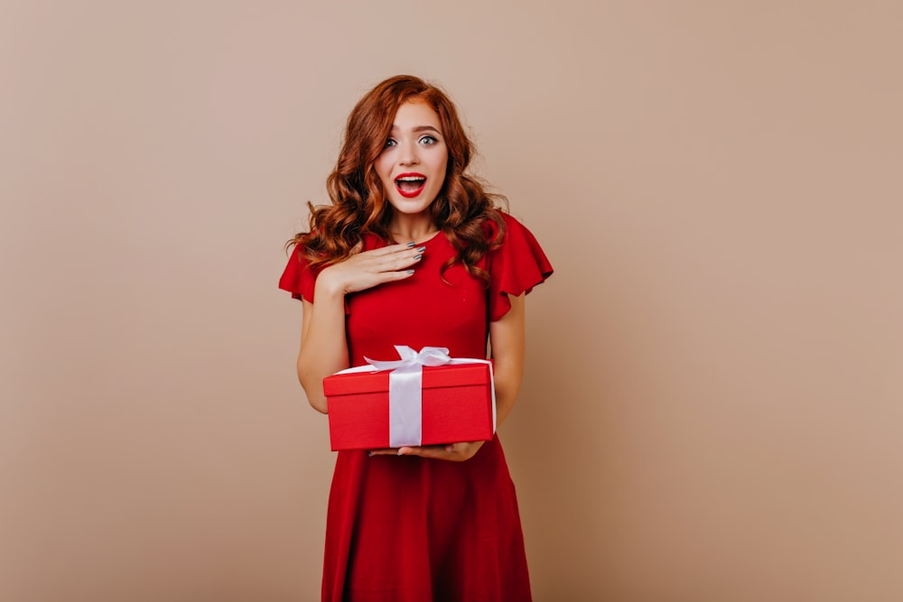 a woman in a red dress holding a red gift box