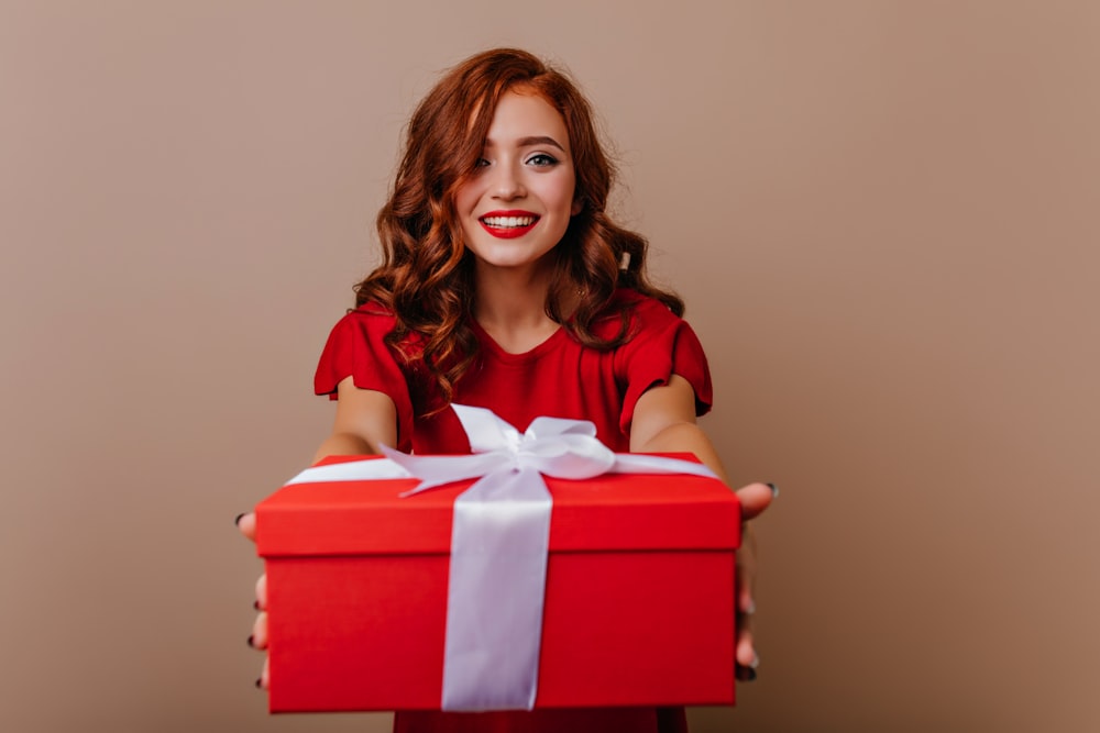 a woman holding a red gift box with a white ribbon