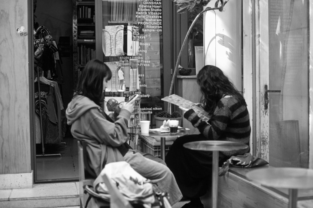 two women sitting at a table in front of a store