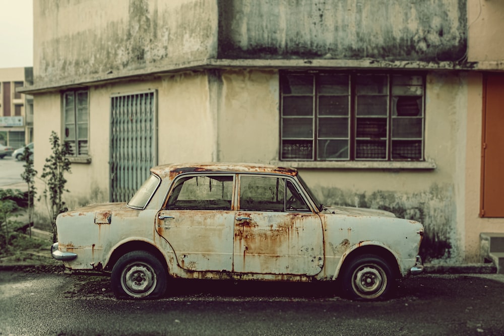 an old rusty car parked in front of a run down building