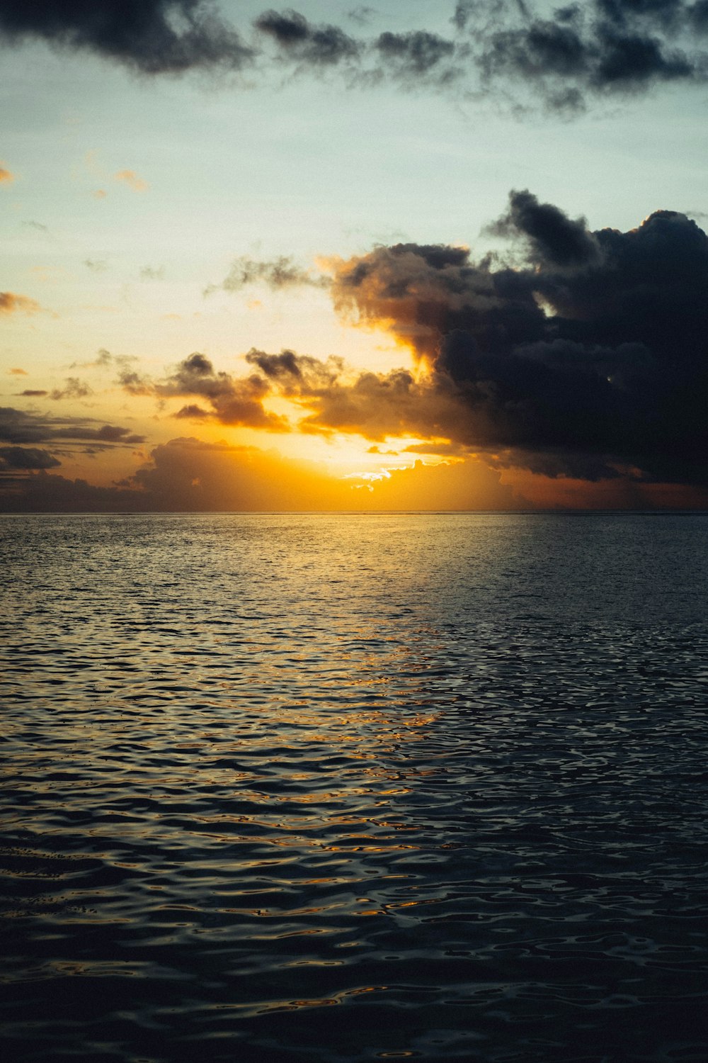 the sun is setting over the ocean on a cloudy day