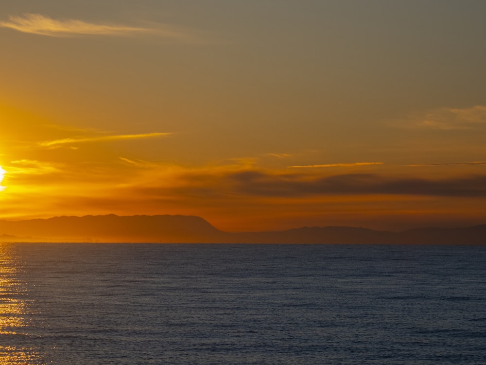 the sun is setting over the ocean with mountains in the distance