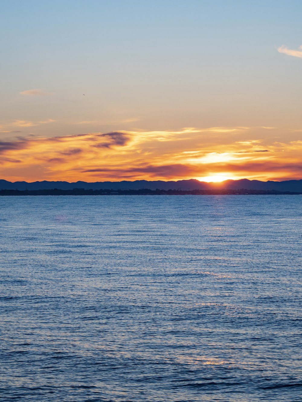 the sun is setting over the ocean with mountains in the distance