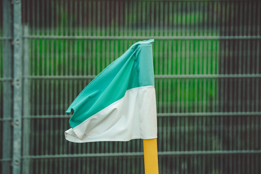 a green and white flag on a pole in front of a fence