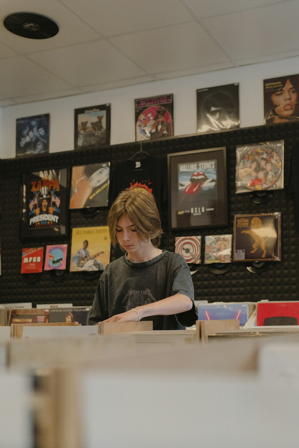 a young man sitting at a table in front of a wall with posters on it