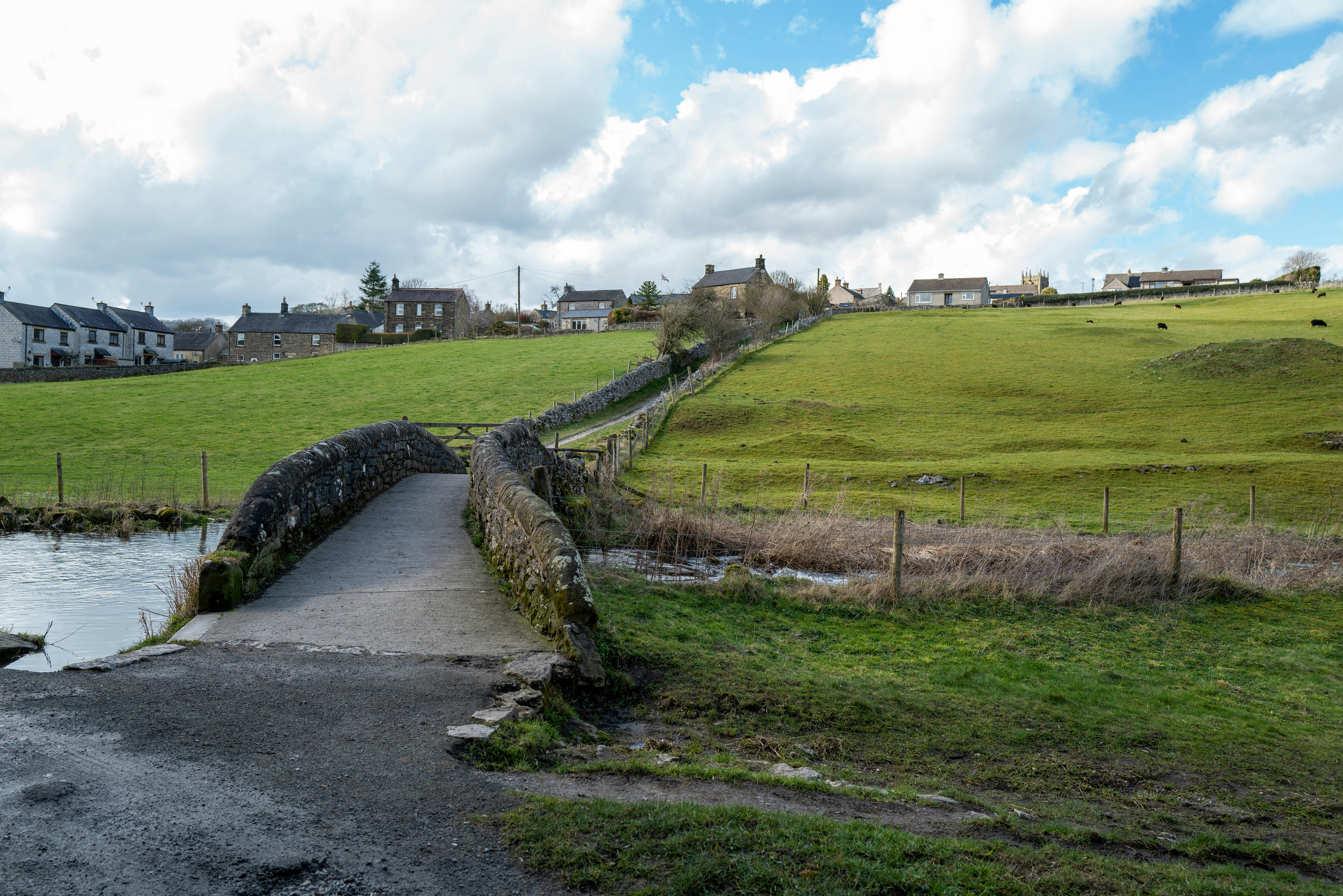 a stone bridge over a stream in a green field, 