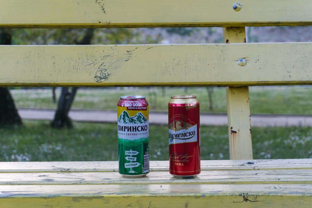 a couple of cans of soda sitting on top of a wooden bench