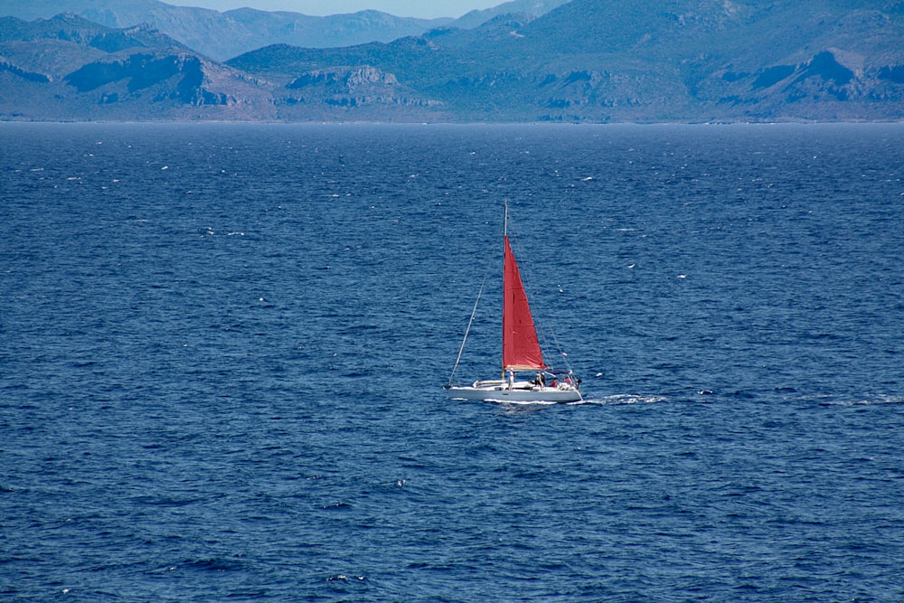 a red sailboat in the middle of a large body of water