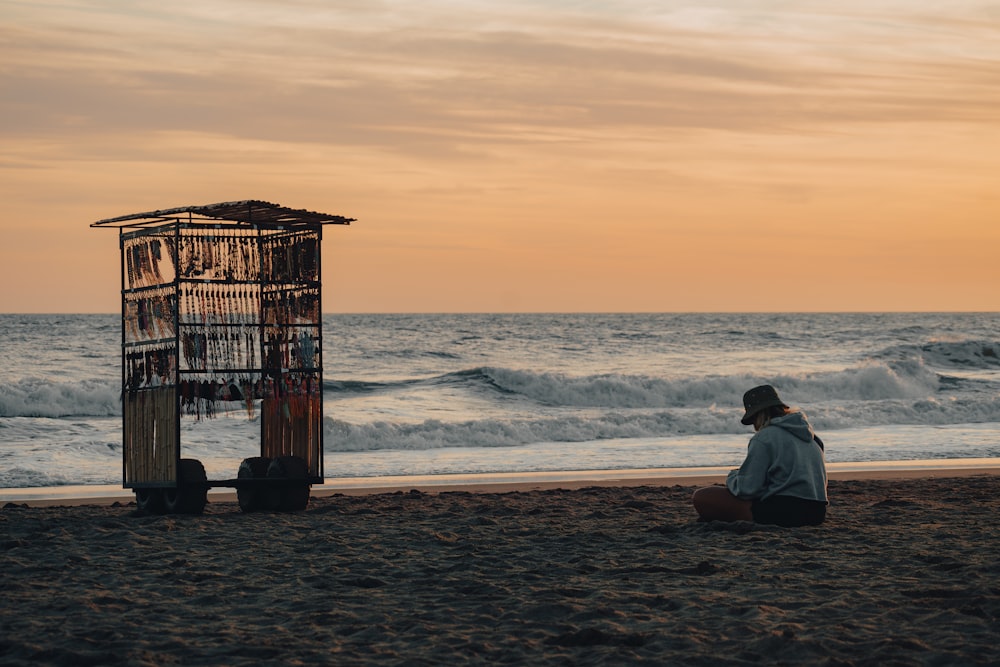 a person sitting on a beach next to a birdcage
