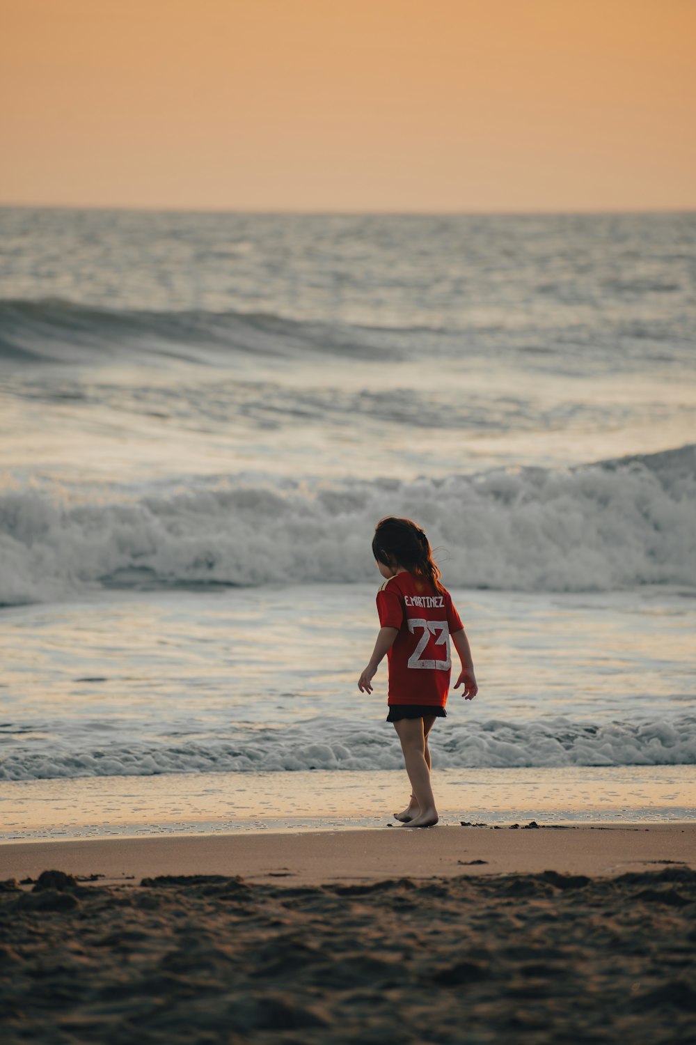 a little girl standing on top of a beach next to the ocean