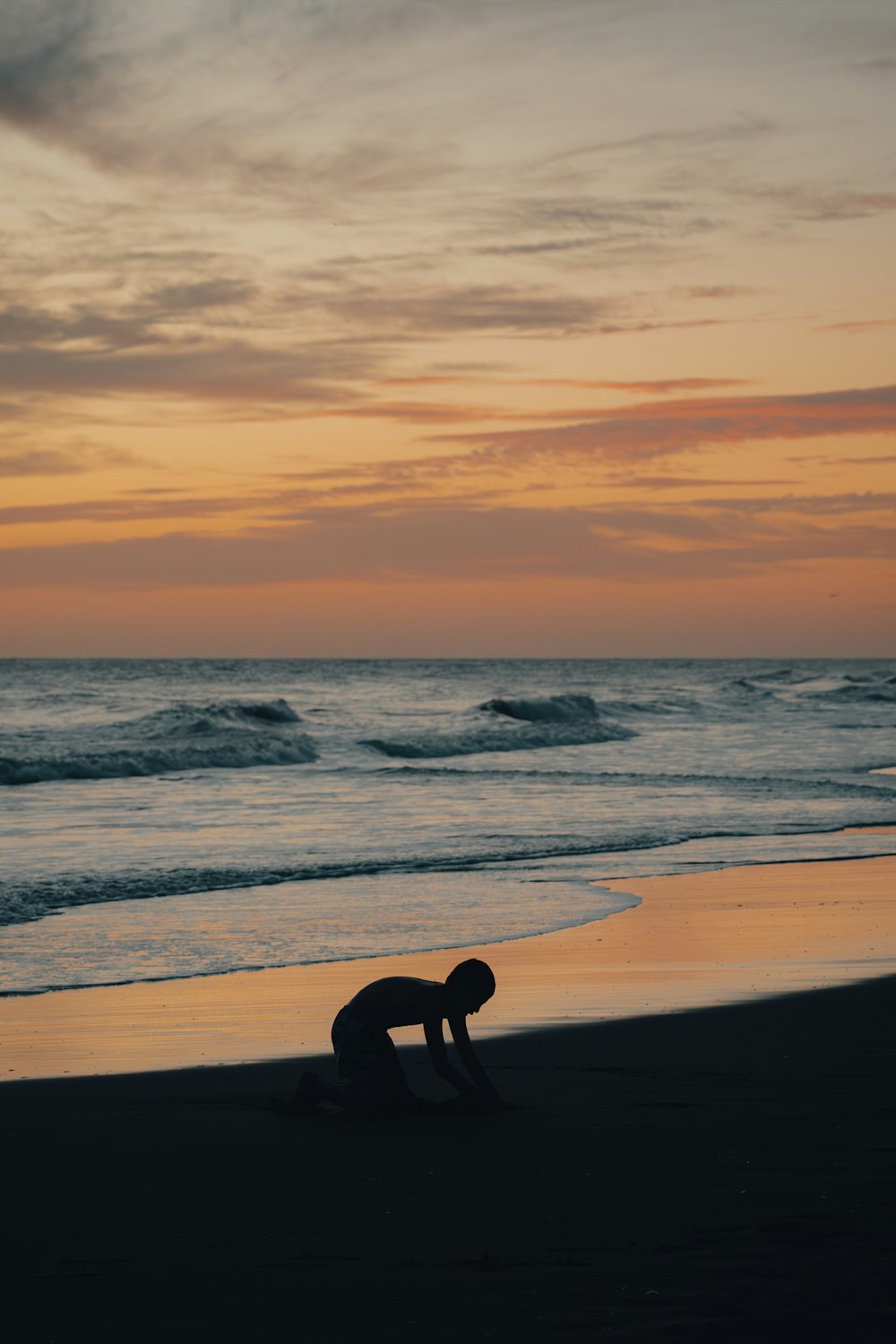 a person kneeling down on a beach next to the ocean