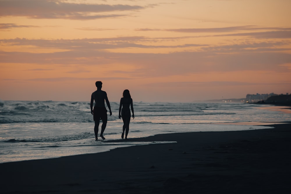 a man and a woman walking on the beach at sunset