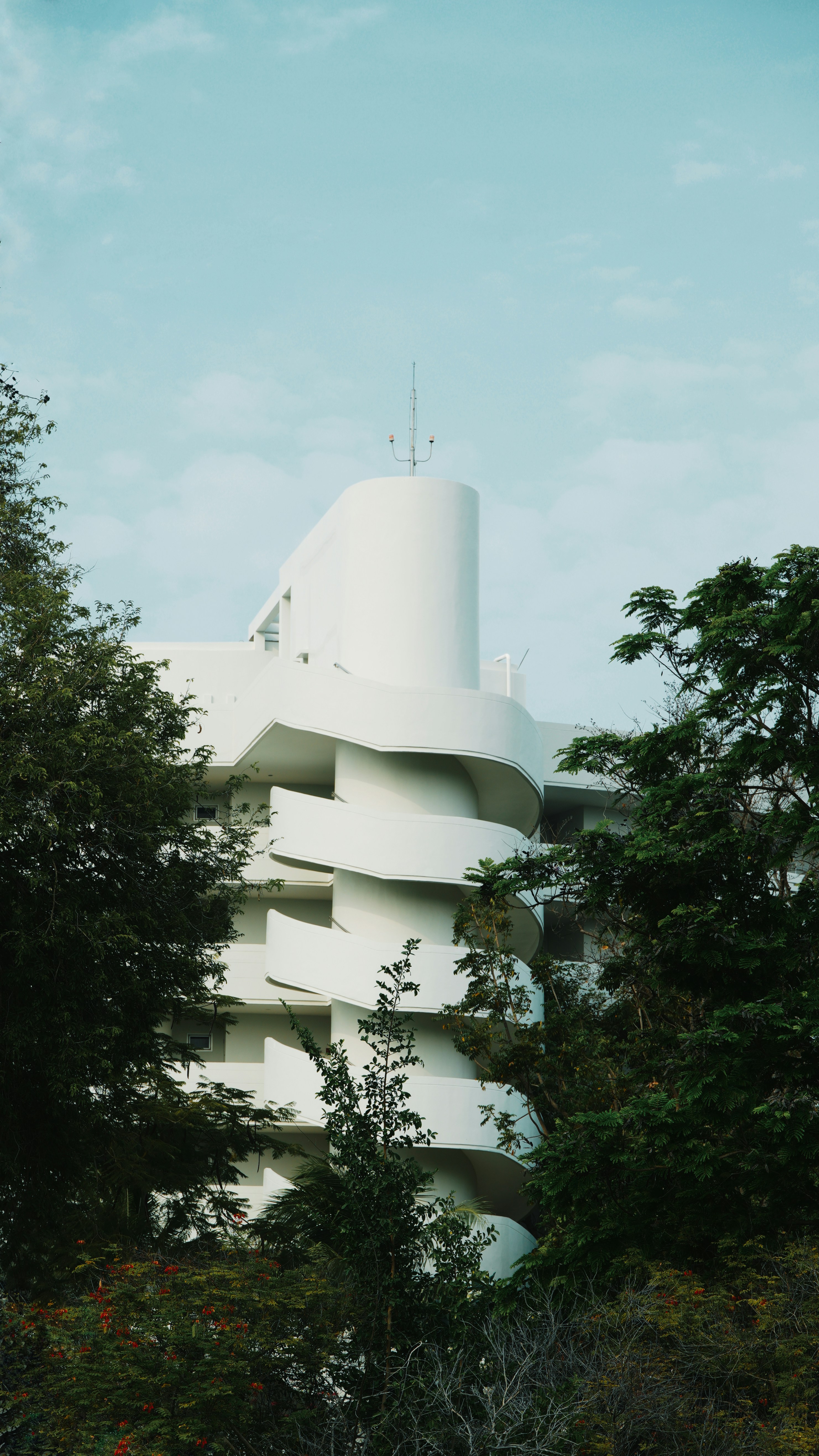 a tall white building surrounded by trees and bushes