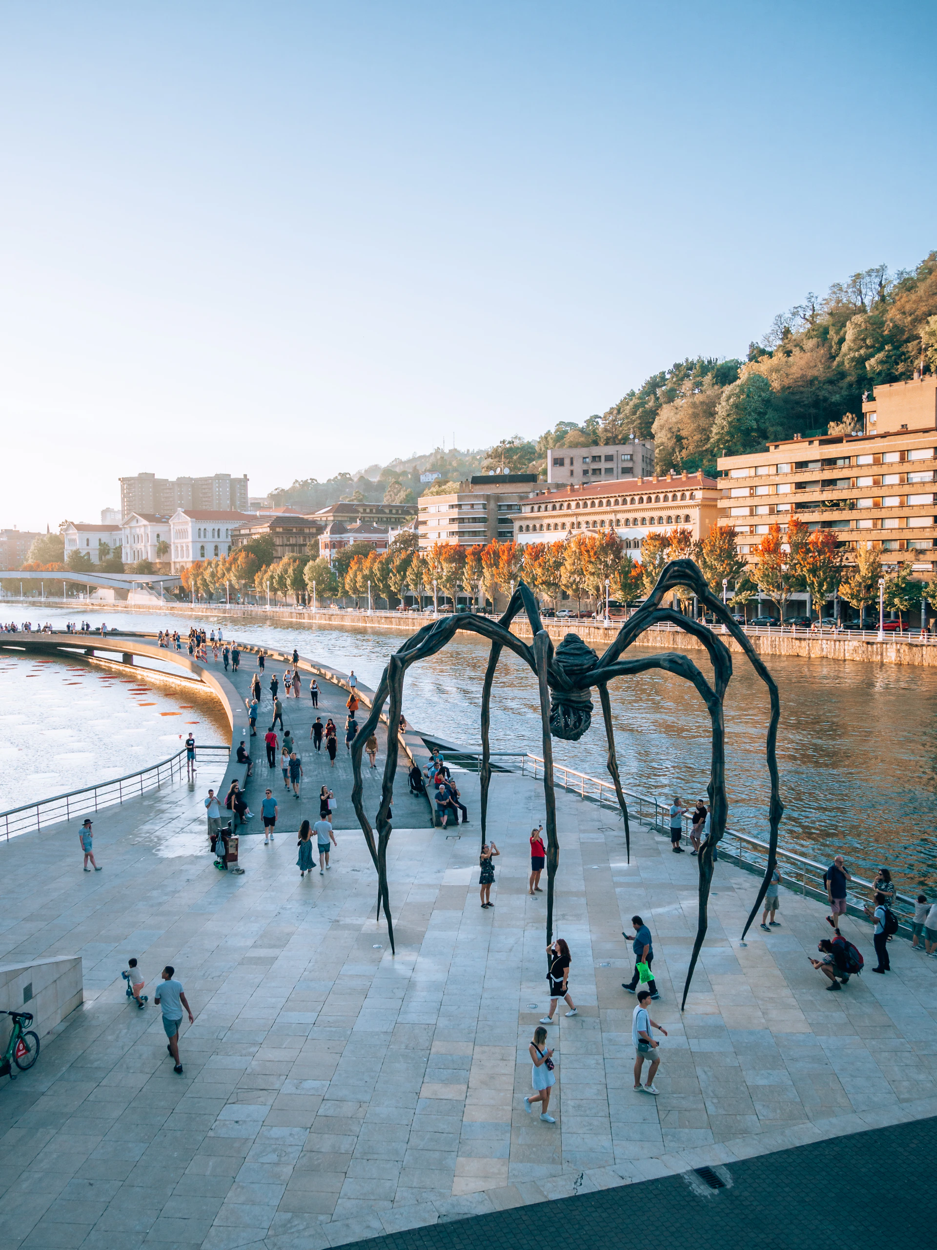 a large spider sculpture sitting on the side of a river