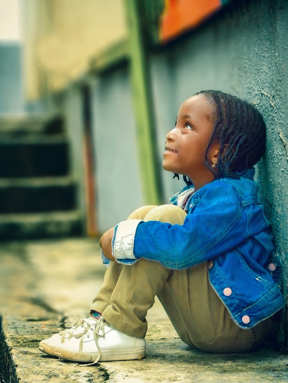 a little girl sitting on the ground next to a wall