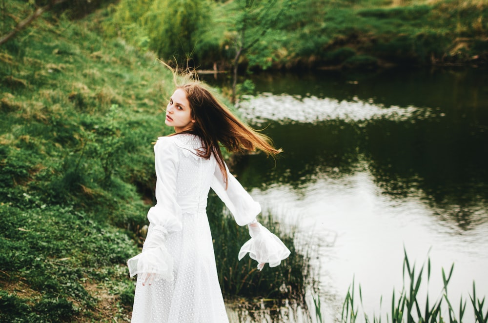 a woman in a white dress standing by a pond