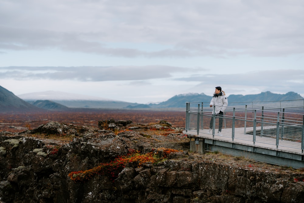 a woman standing on a bridge over a mountain