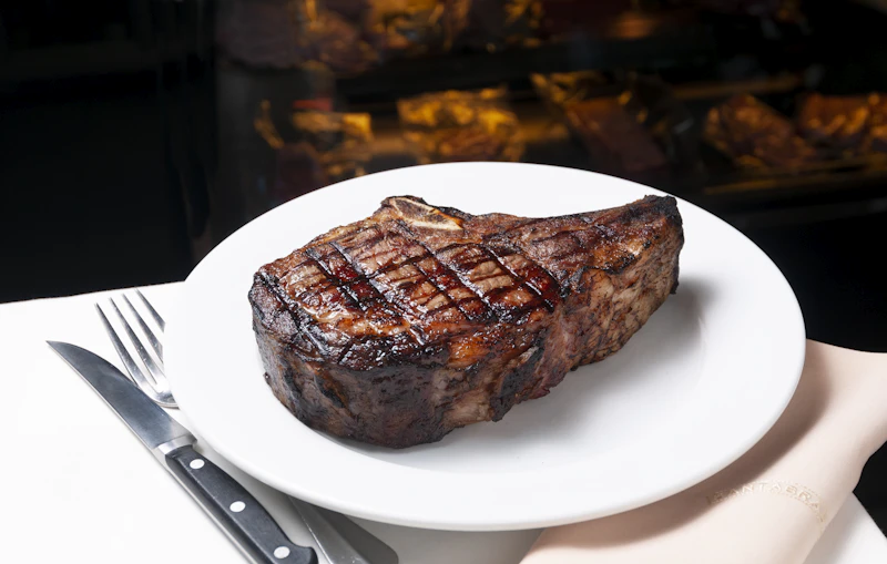 A grilled steak with cross-hatch sear marks served on a white plate with a fork and knife