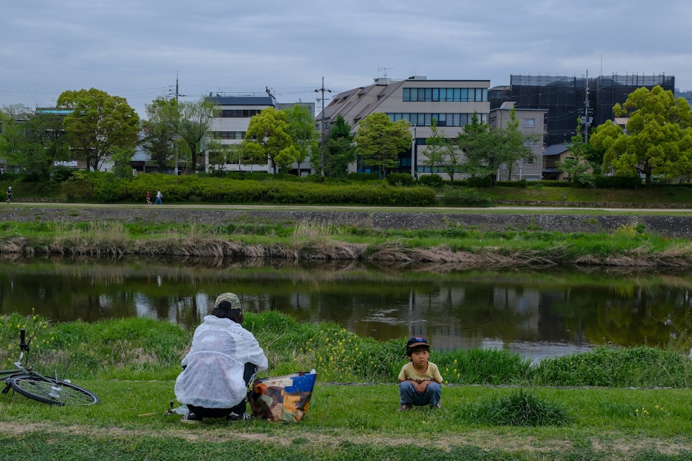 a man and a child sitting on the grass near a river