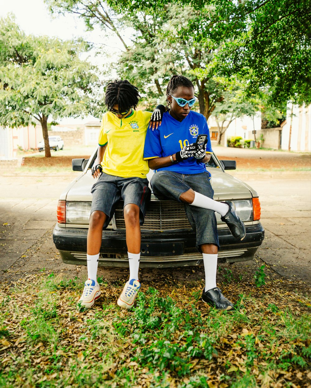 two young men sitting on the hood of a car