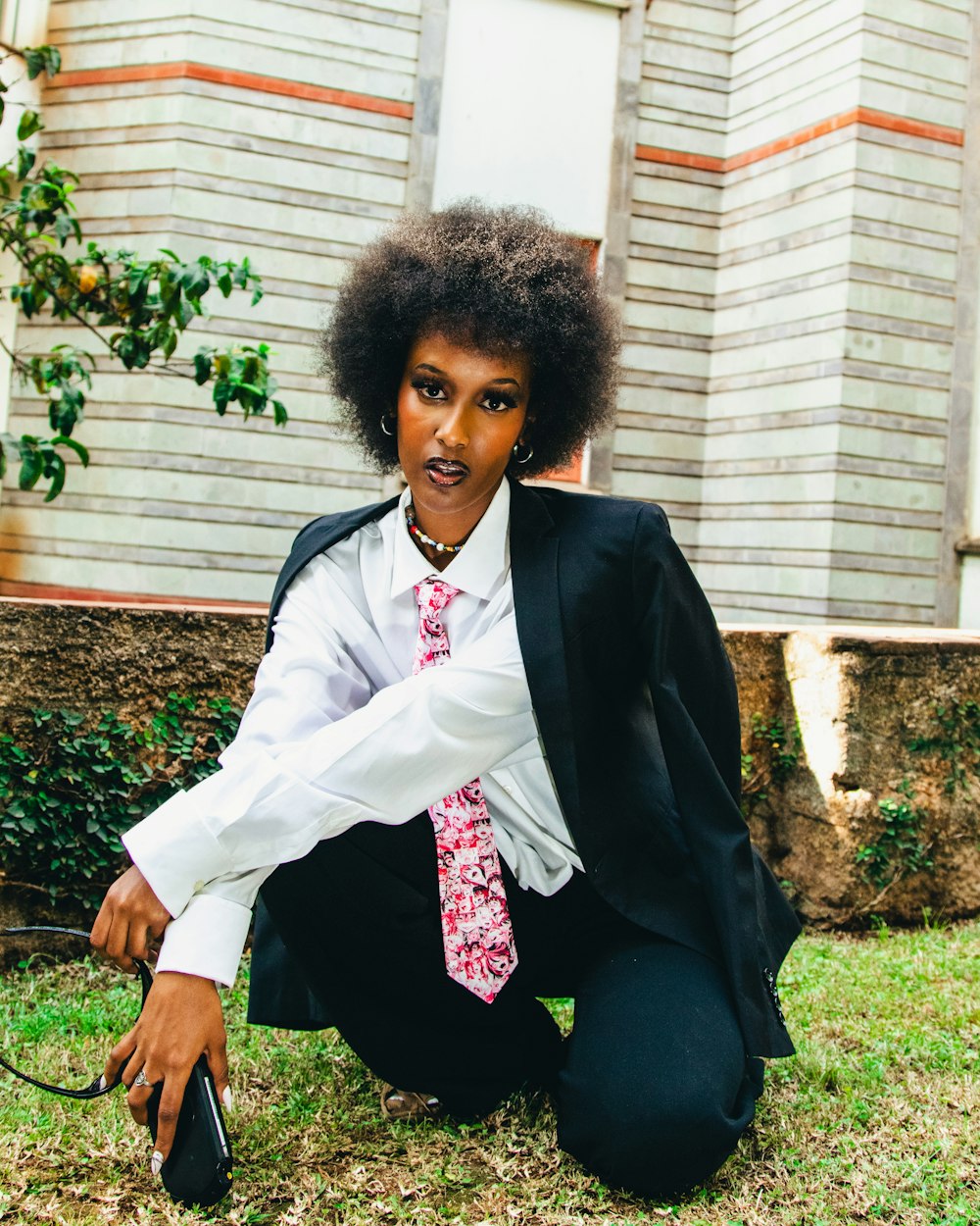 a woman in a suit and tie kneeling on the grass