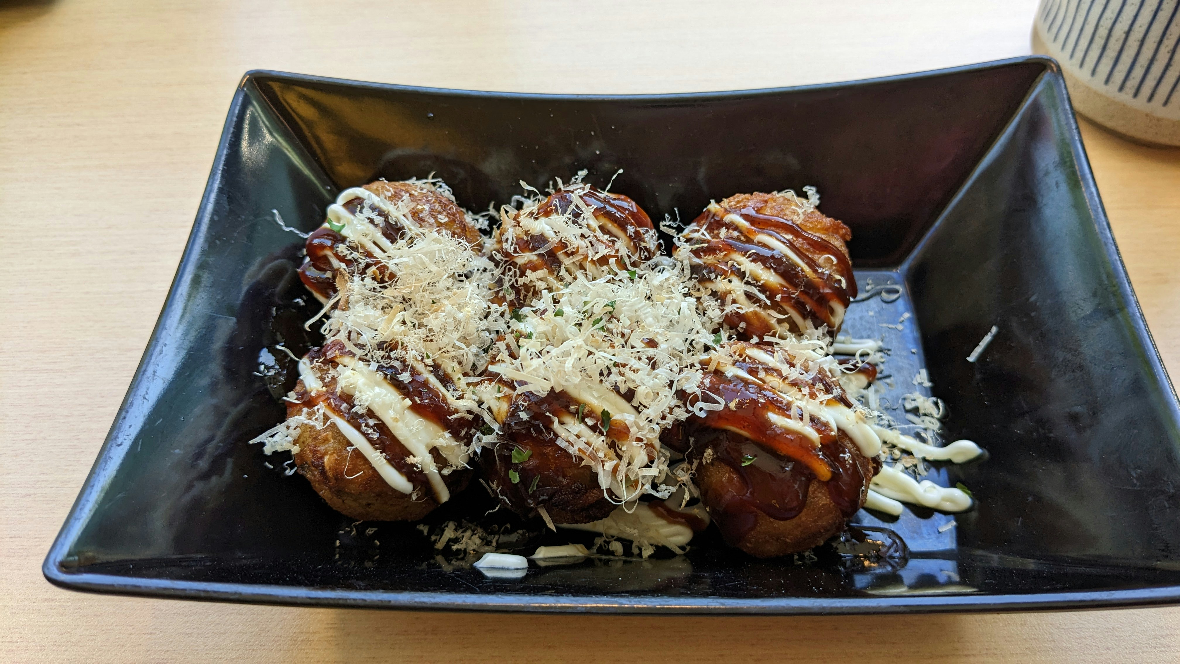 Golden takoyaki octopus balls in a tray topped with bonito flakes and drizzled with dark sauce, dark moody background
