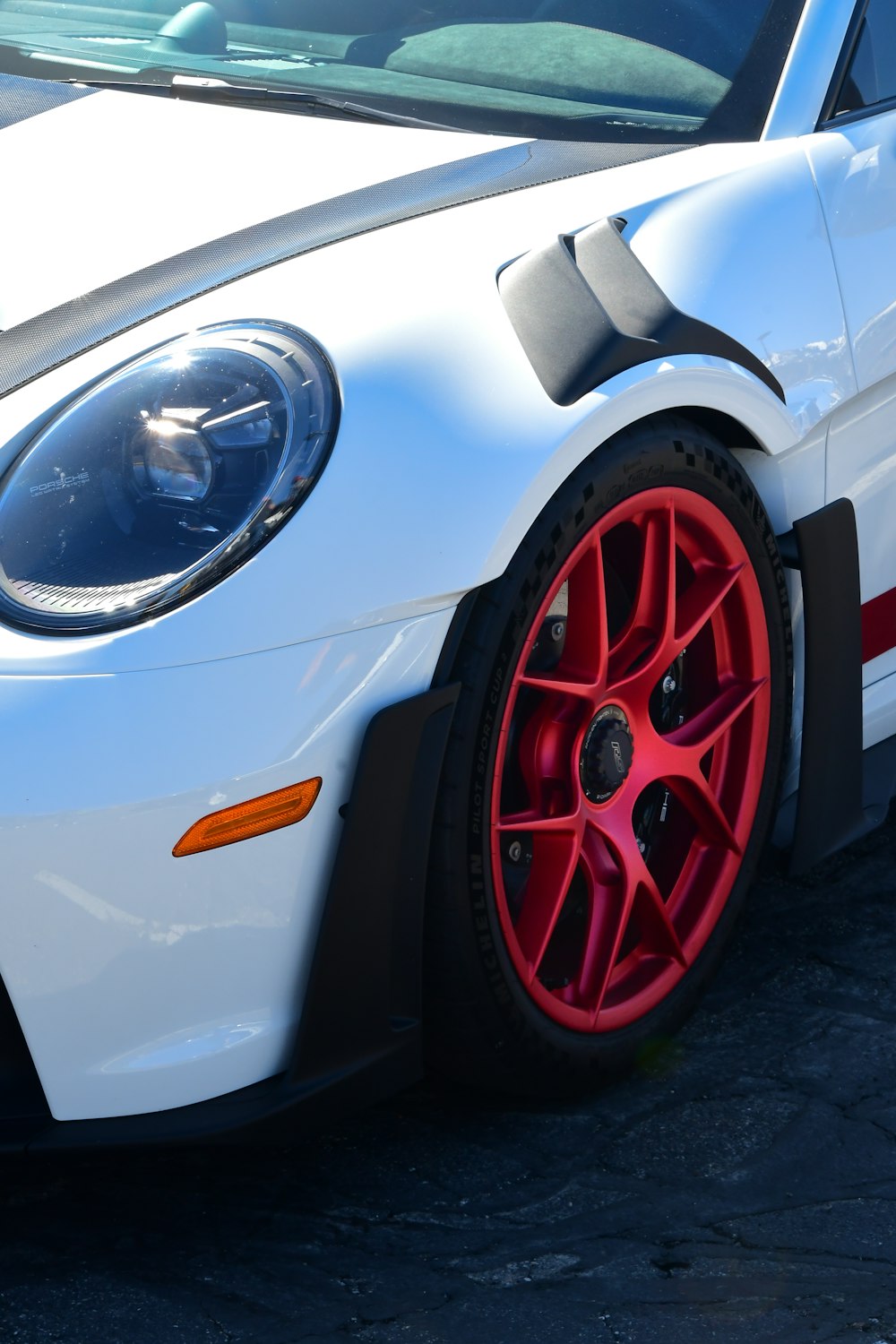 a white sports car with red rims parked in a parking lot
