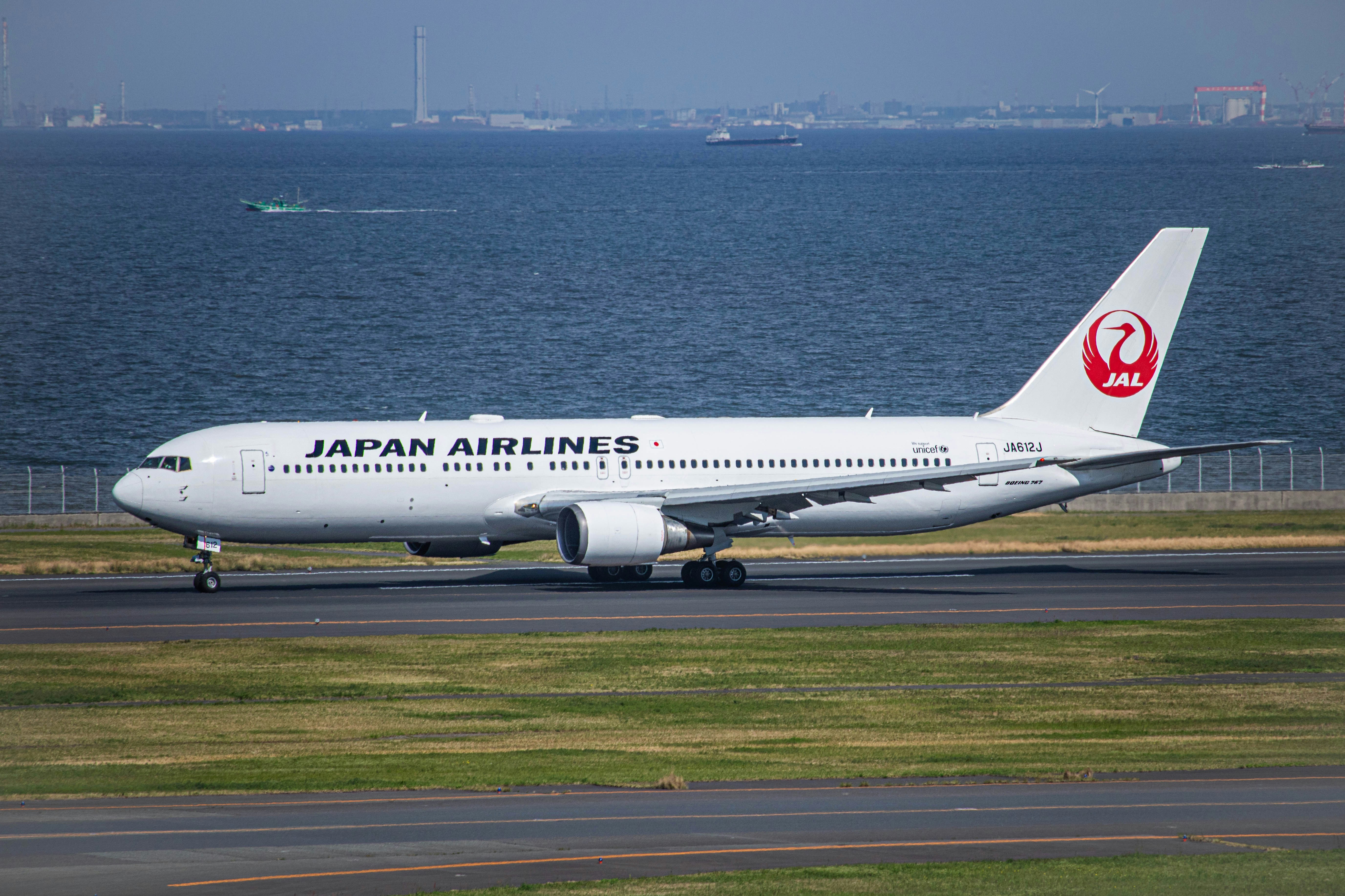 a japan airlines plane on a runway near the water, 