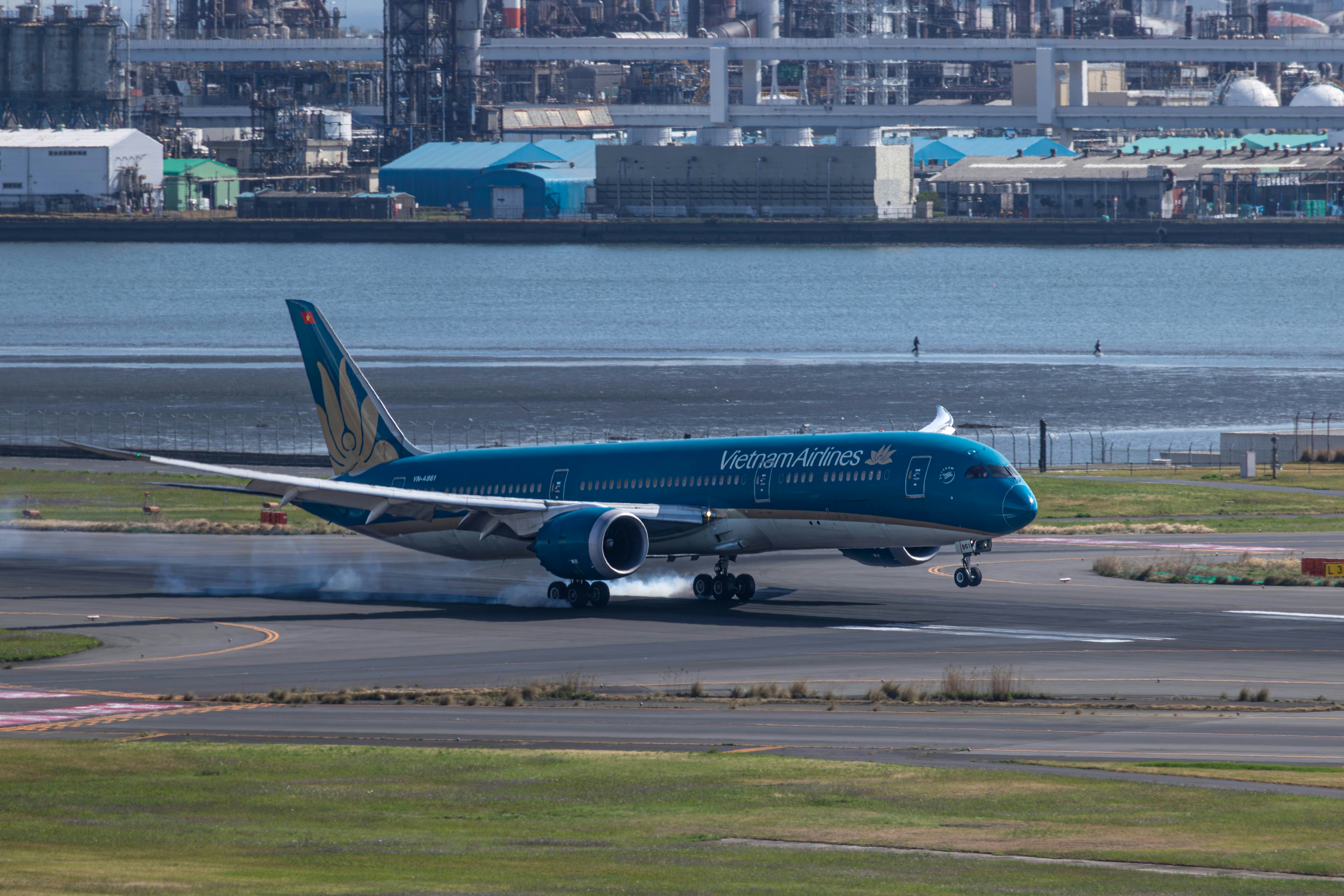 a blue and white jet airliner on runway next to water, 