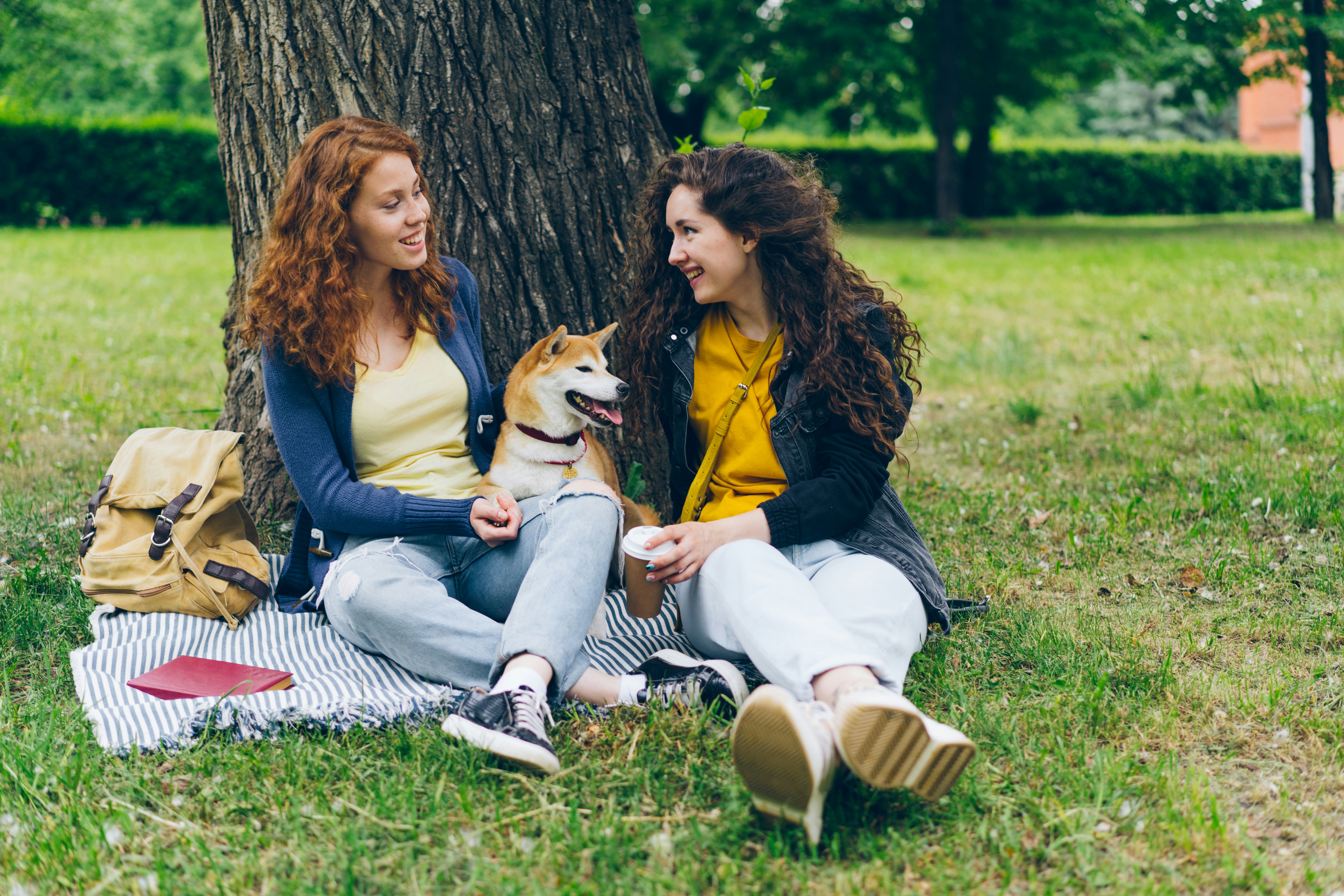 two women sitting on a blanket next to a tree