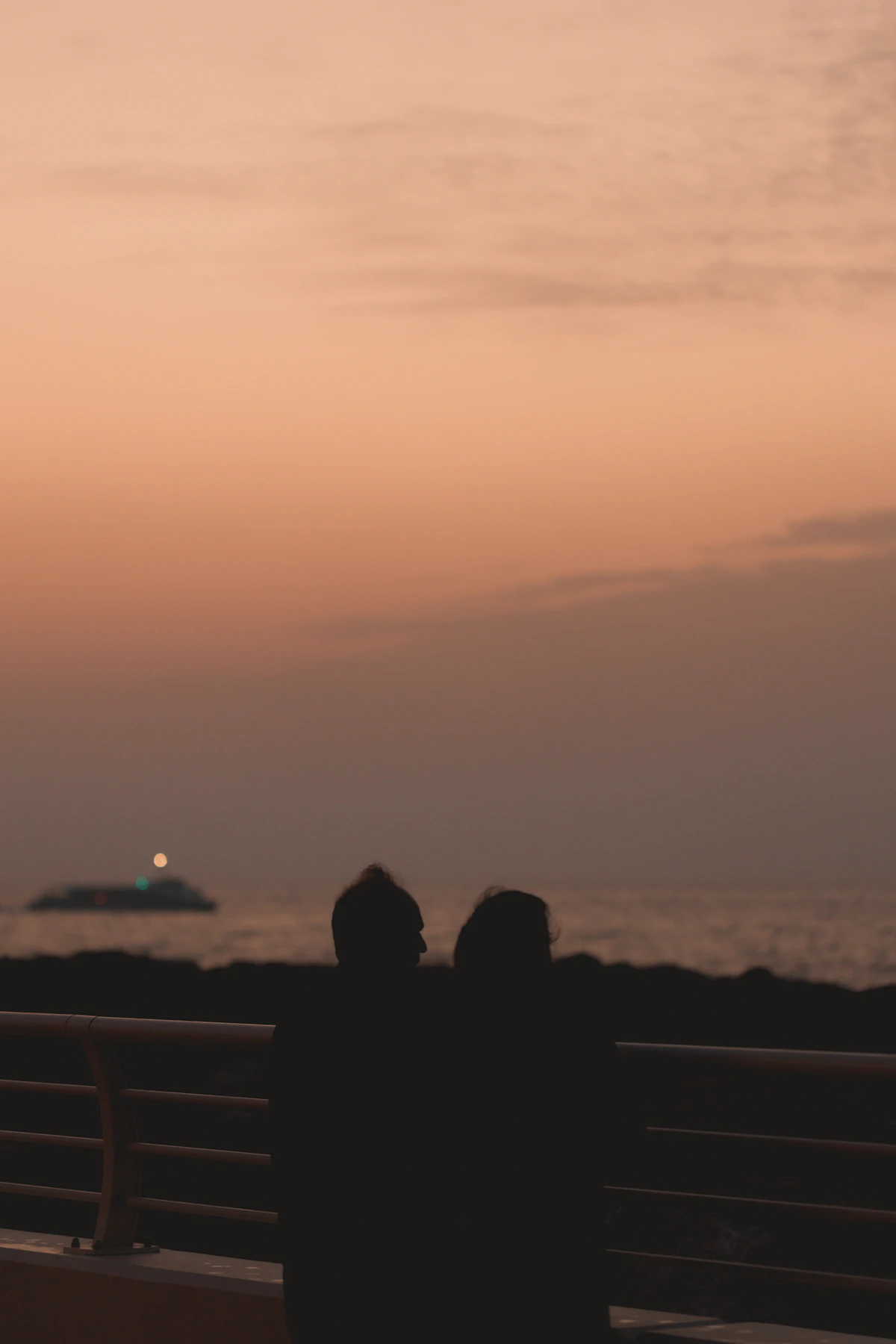 Two people sitting on a bench by the sea at sunset in Dubai