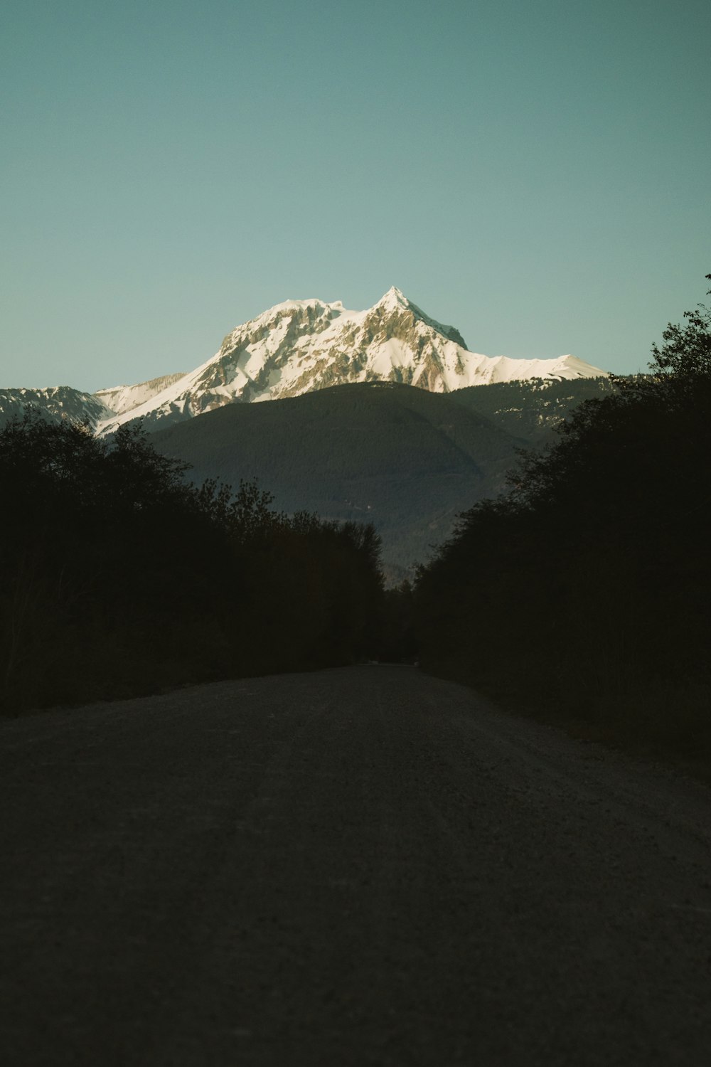 a dirt road with a snow covered mountain in the background