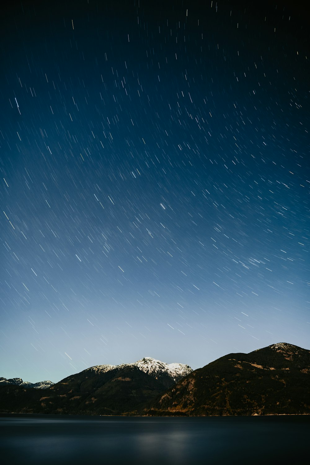 el cielo nocturno sobre una cadena montañosa y un cuerpo de agua