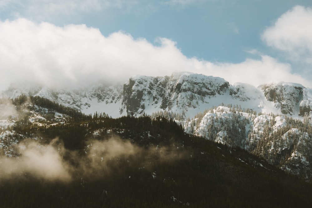 a mountain covered in snow and clouds under a blue sky