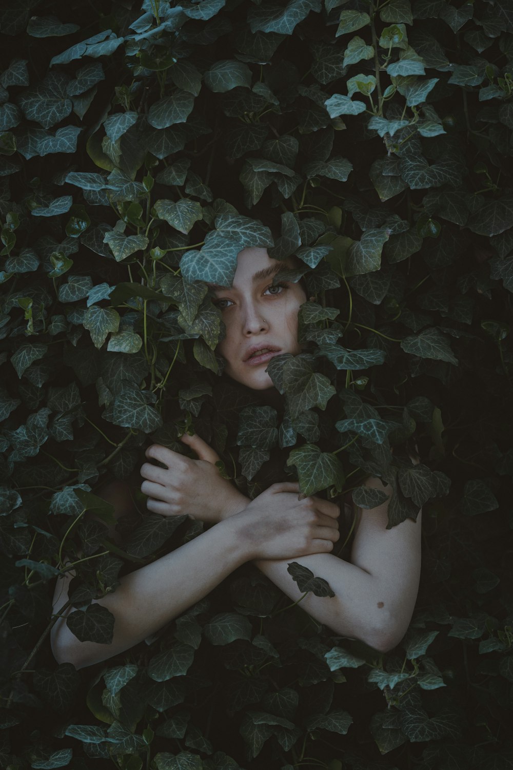 a woman hiding behind a bush with her hands on her chest