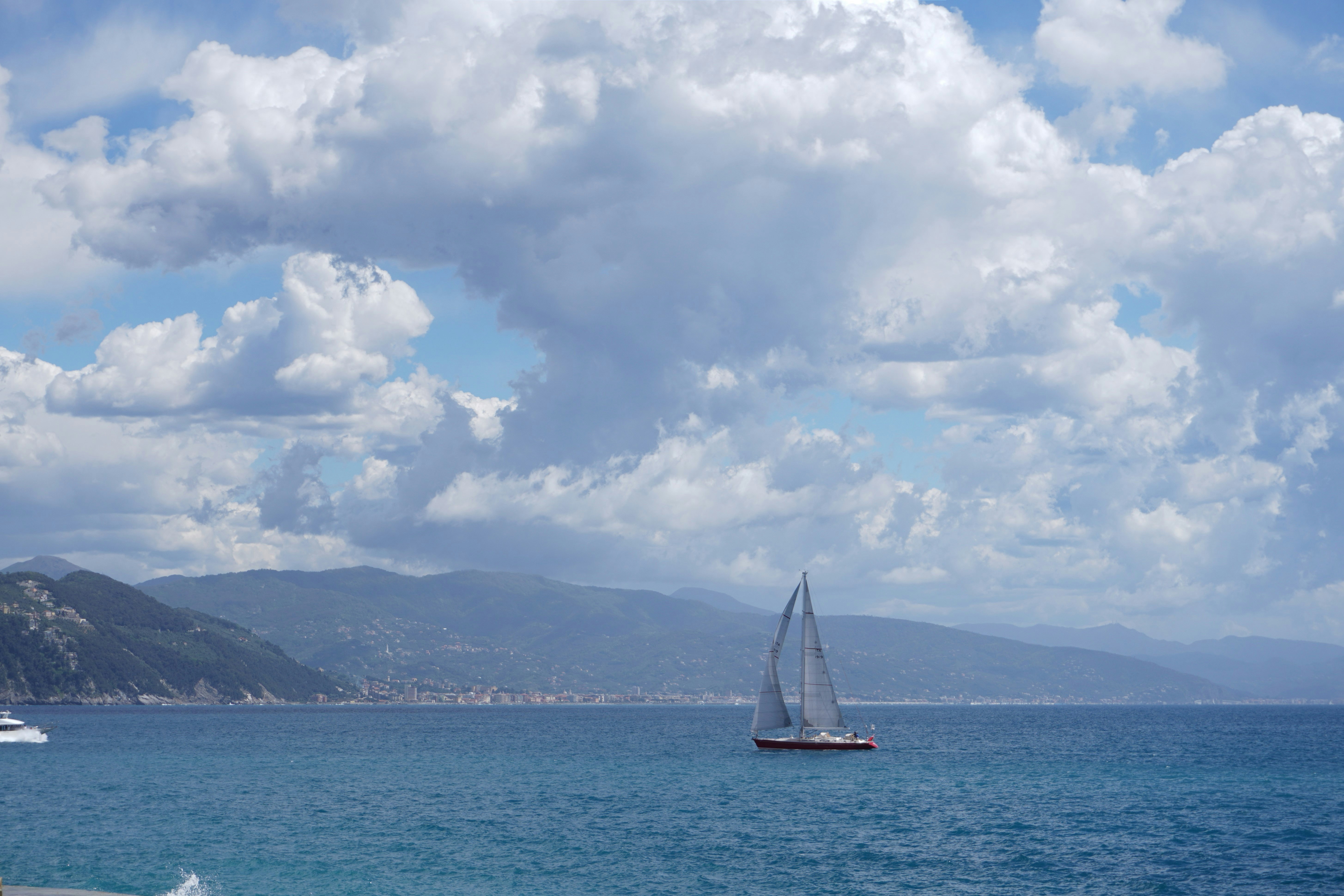 a sailboat sailing on a large body of water, Panorama view of the seaside city, mountains on the horizon, Portofino