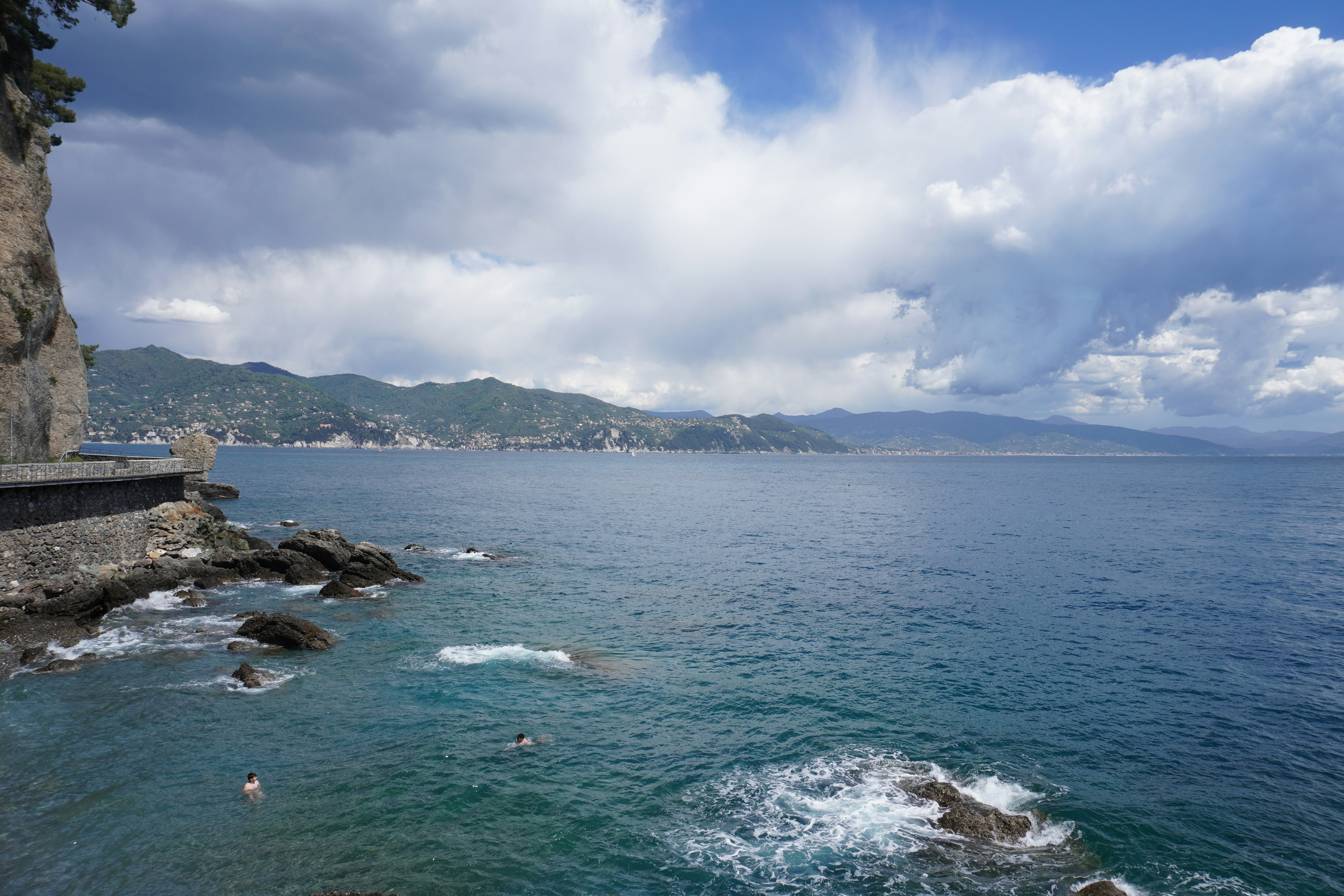 a body of water with people swimming in it, Panorama view of the seaside city, mountains on the horizon, Portofino