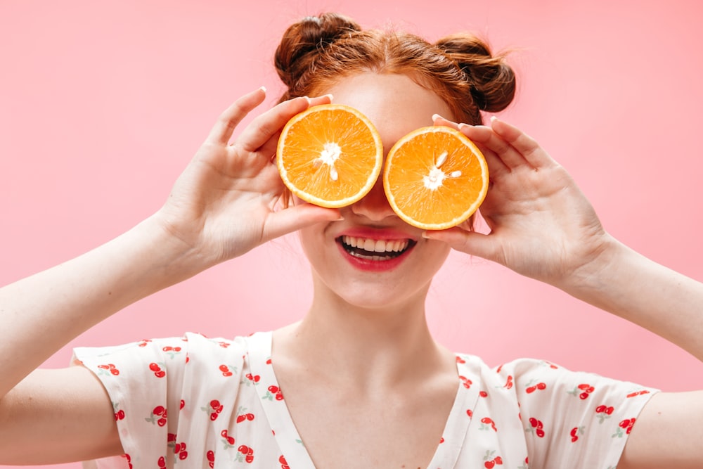 a woman holding two slices of oranges in front of her eyes