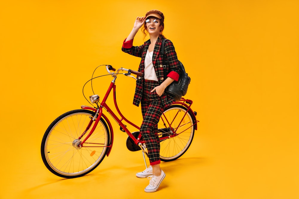 a woman standing next to a red bike on a yellow background