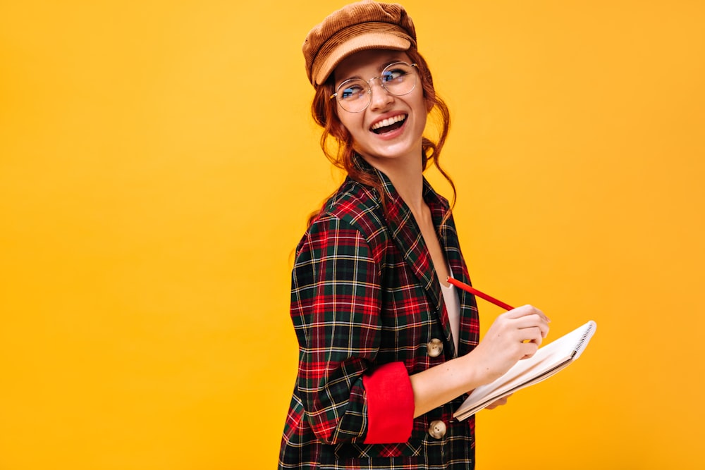 a woman wearing glasses and a hat holding a book