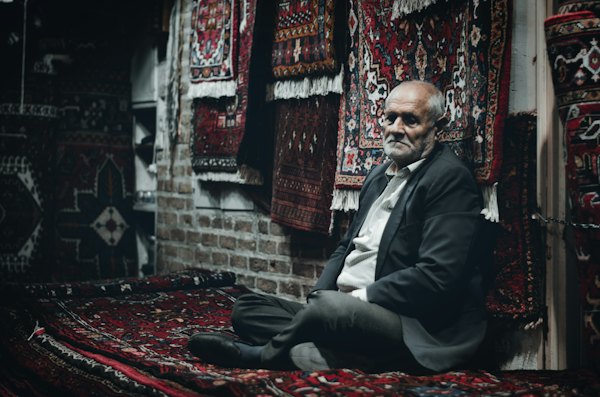 A carpet seller among his rugs in the bazaar — Tabriz, Iran