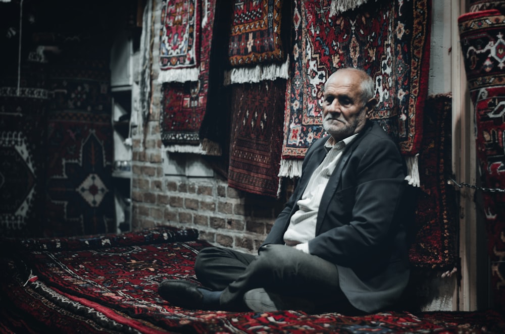 a man sitting on a rug in a room filled with rugs