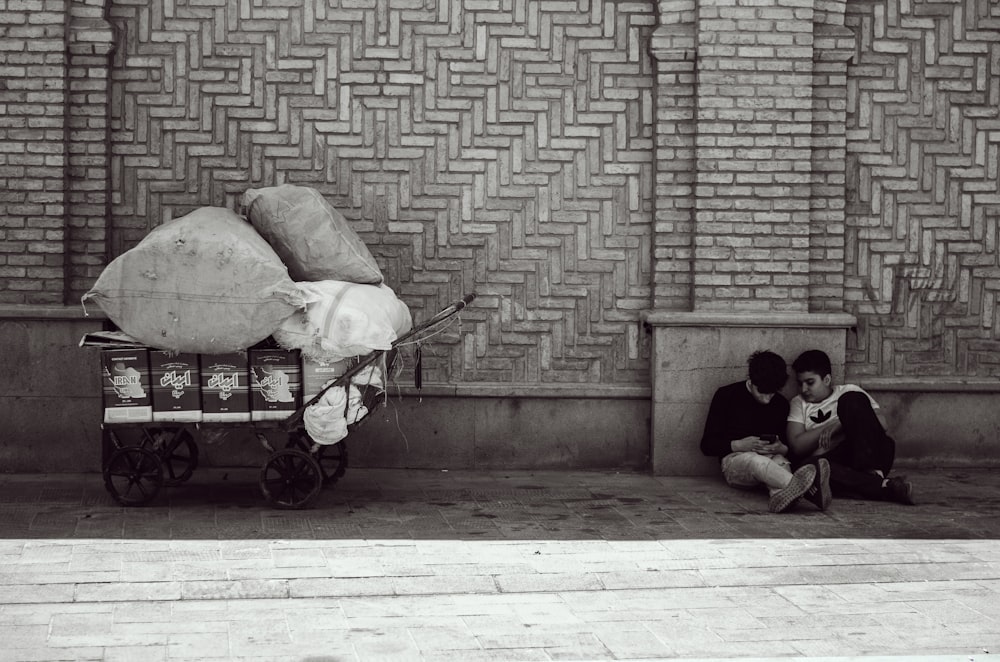 two people sitting on the ground next to a brick wall