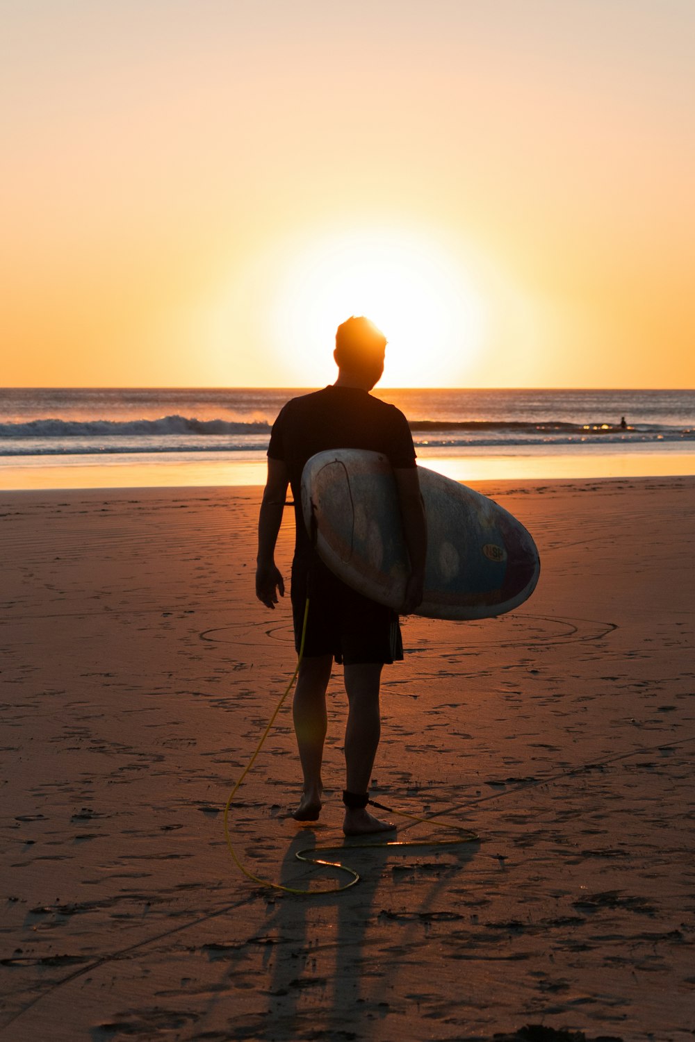 Un homme tenant une planche de surf au sommet d’une plage de sable