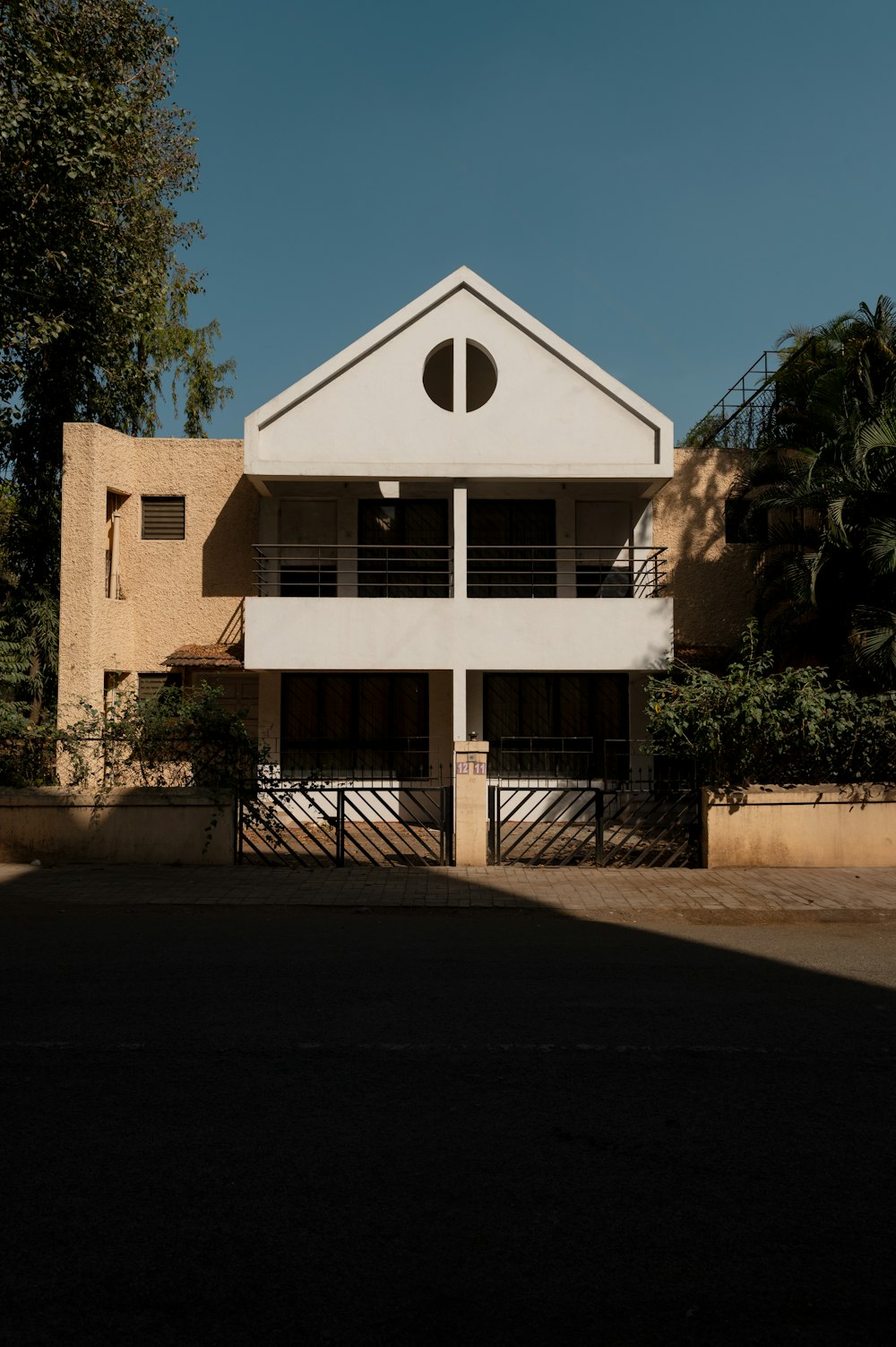 a white building with a black gate and trees in the background