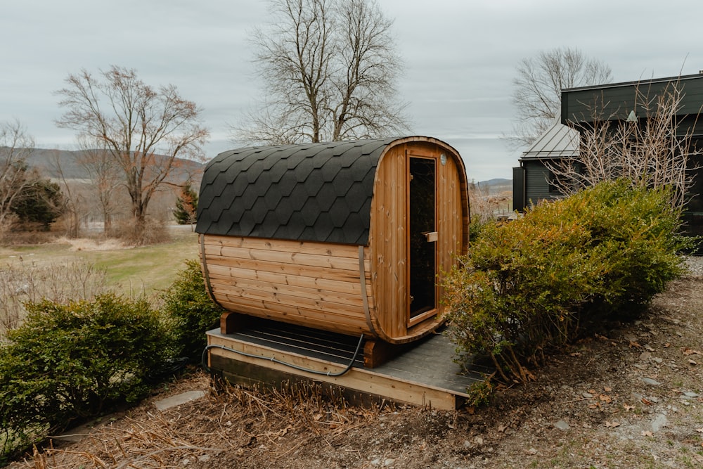 a wooden outhouse sitting in a field next to a bush