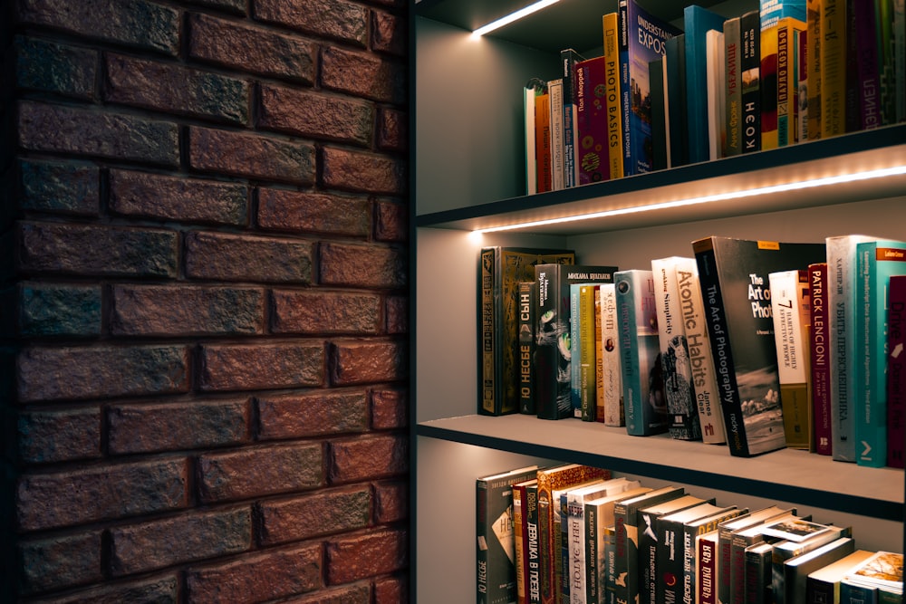 a bookshelf filled with lots of books next to a brick wall