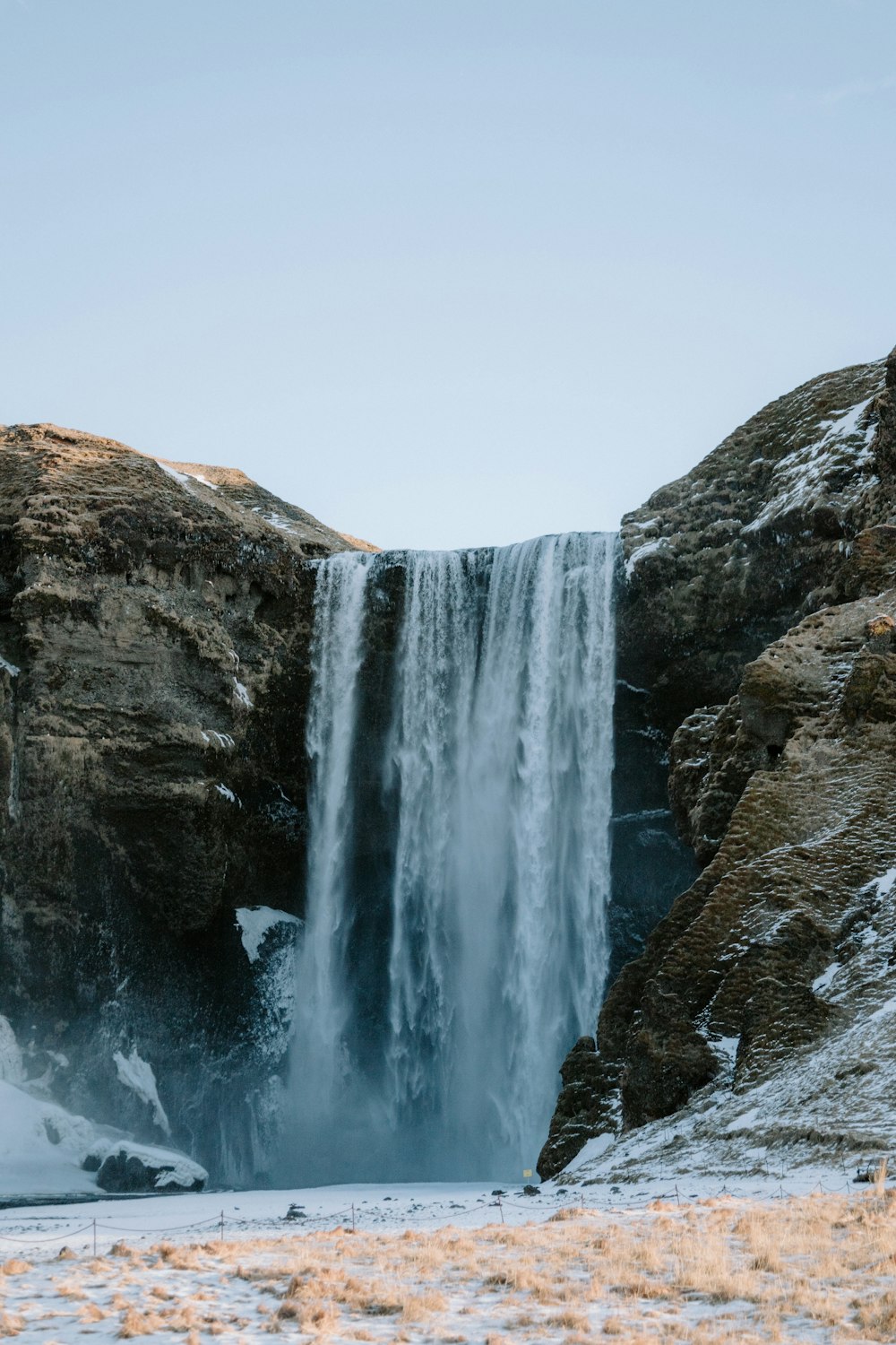 a large waterfall with snow on the ground