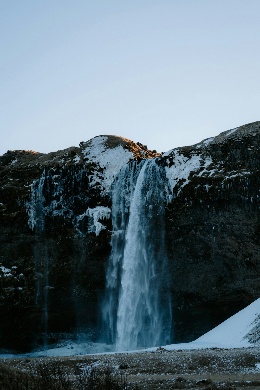 a large waterfall with snow on the ground