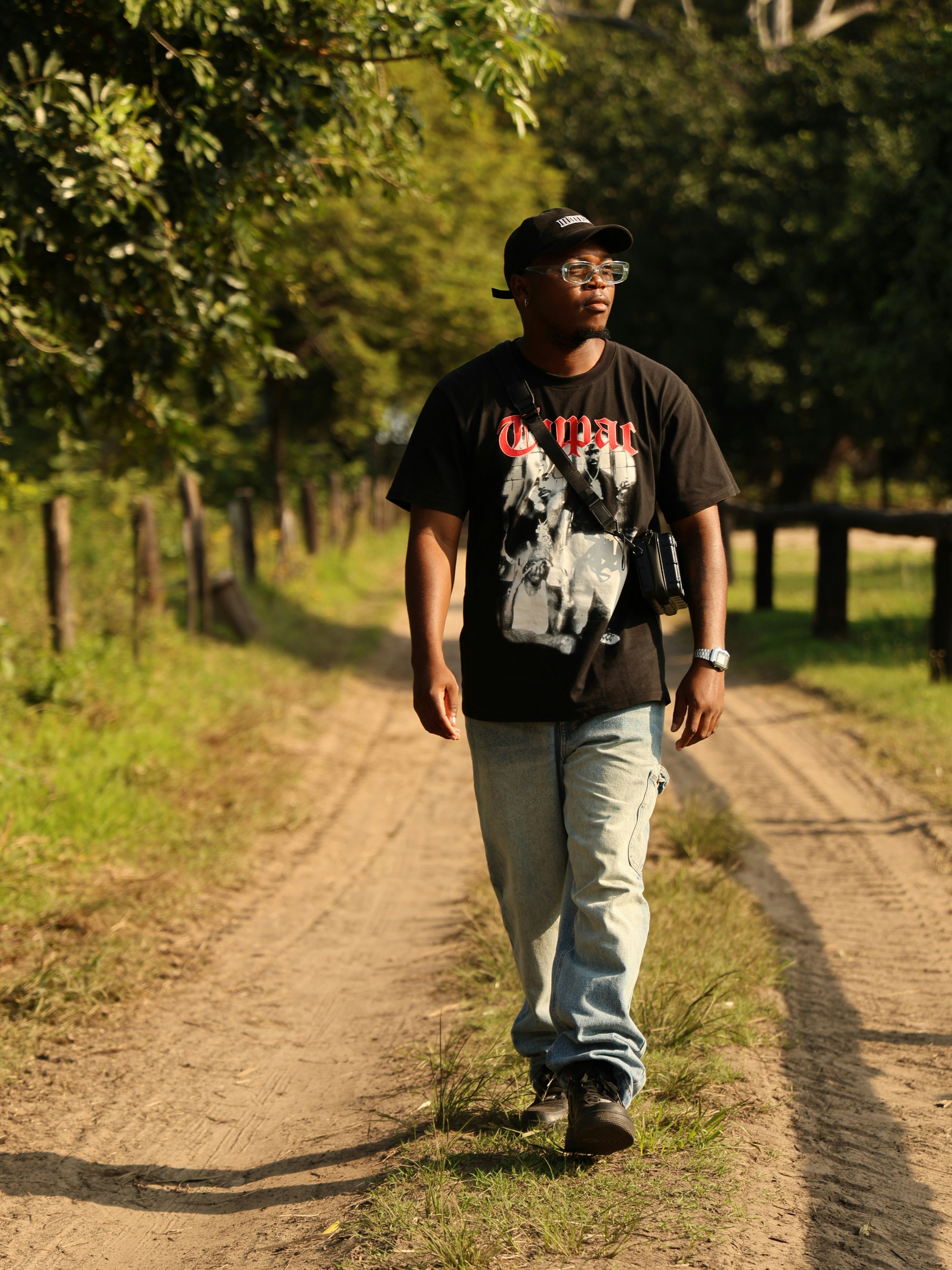 a man walking down a dirt road next to a forest